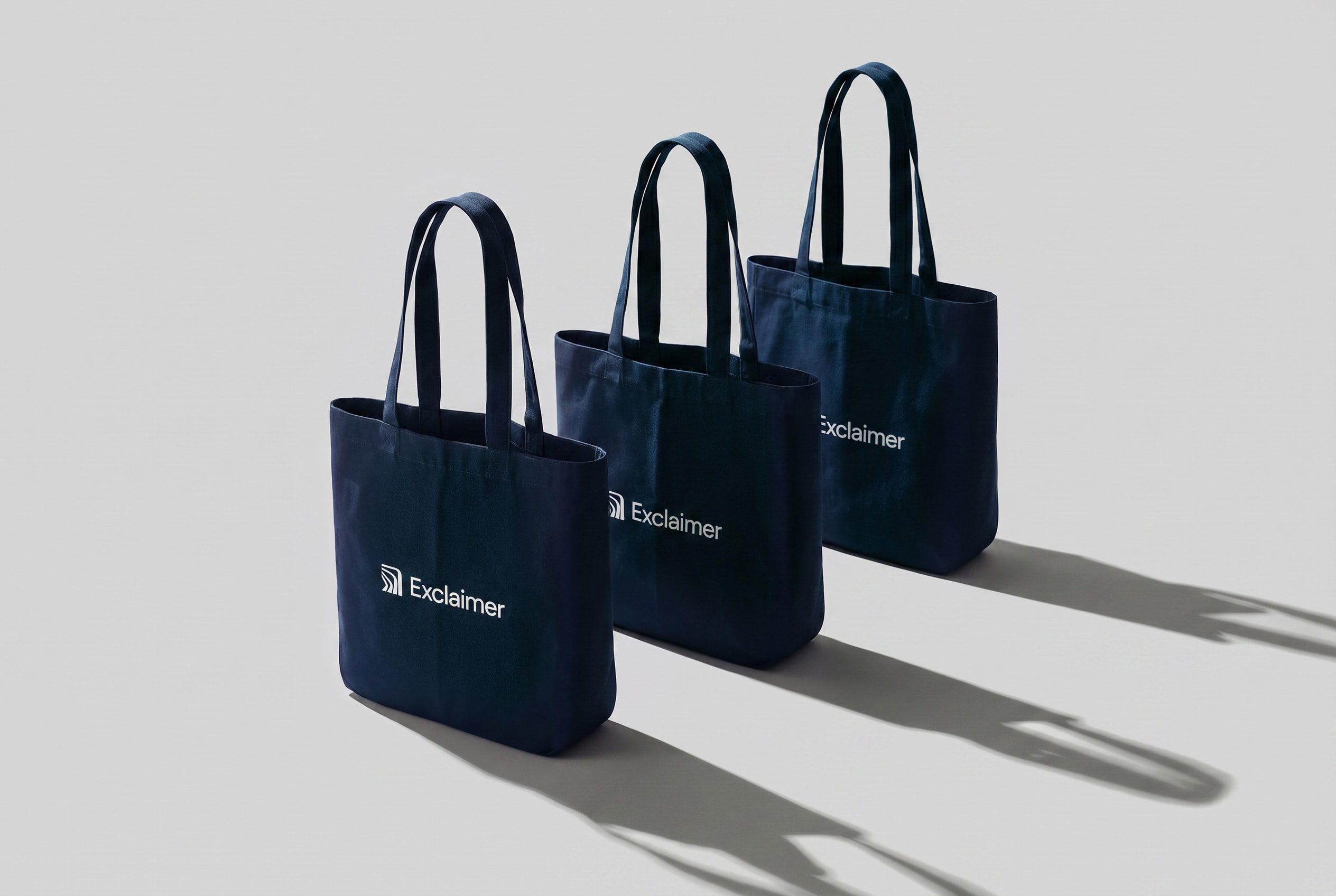 Three navy Exclaimer tote bags in directional studio light